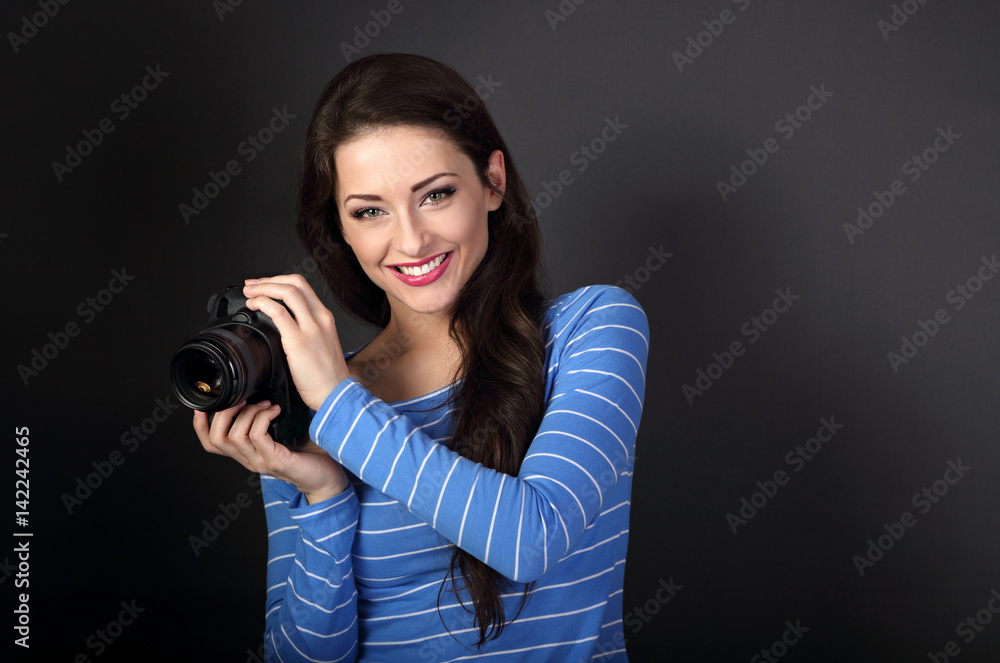 Toothy smiling female photograph holding photo camera and looking happy on dark grey background with empty copy space. Closeup portrait Toothy smiling female photograph holding photo camera and looking happy on dark grey background with empty copy space. Closeup portrait