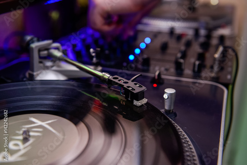 Turntable playing vinyl close up with needle on the record and playing dj on the background. Selective focus photo