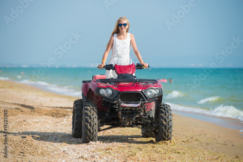 Young girl in sunglasses и платье is riding an ATV on the beach