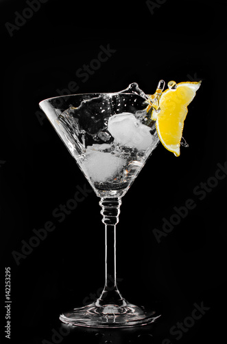 A glass with vermouth and ice cube on a black background