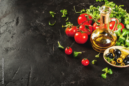 Ingredients of Italian cuisine. Selection of products for salad. Olive oil  lettuce leaves  tomatoes. On a black dark shale concrete stone kitchen table. copy space