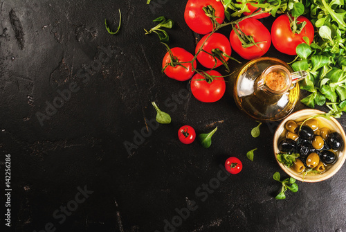 Ingredients of Italian cuisine. Selection of products for salad. Olive oil, lettuce leaves, tomatoes. On a black dark shale concrete stone kitchen table. copy space top view