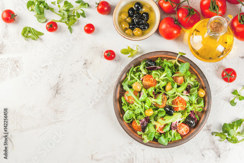 Italian Cuisine. Spring vegan diet food. Fresh lettuce, greens, tomatoes, green and black olives. With fresh organic home-made oil, raw ingredients on the table. Copy space top view