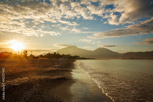 Sea shore in sunshine on background of mountains and sunset sky