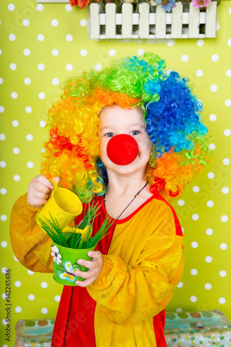 Funny clown watering a watering can with grass in a pot on a bright green background in polka dots