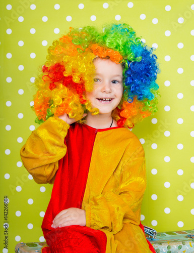 A cheerful clown in an iridescent wig and huge boots stands on a luscious bright green background in polka dots