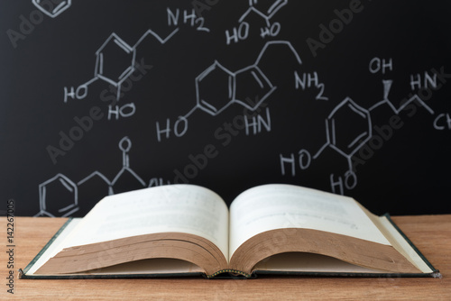 open book on wooden table with science formula on black background