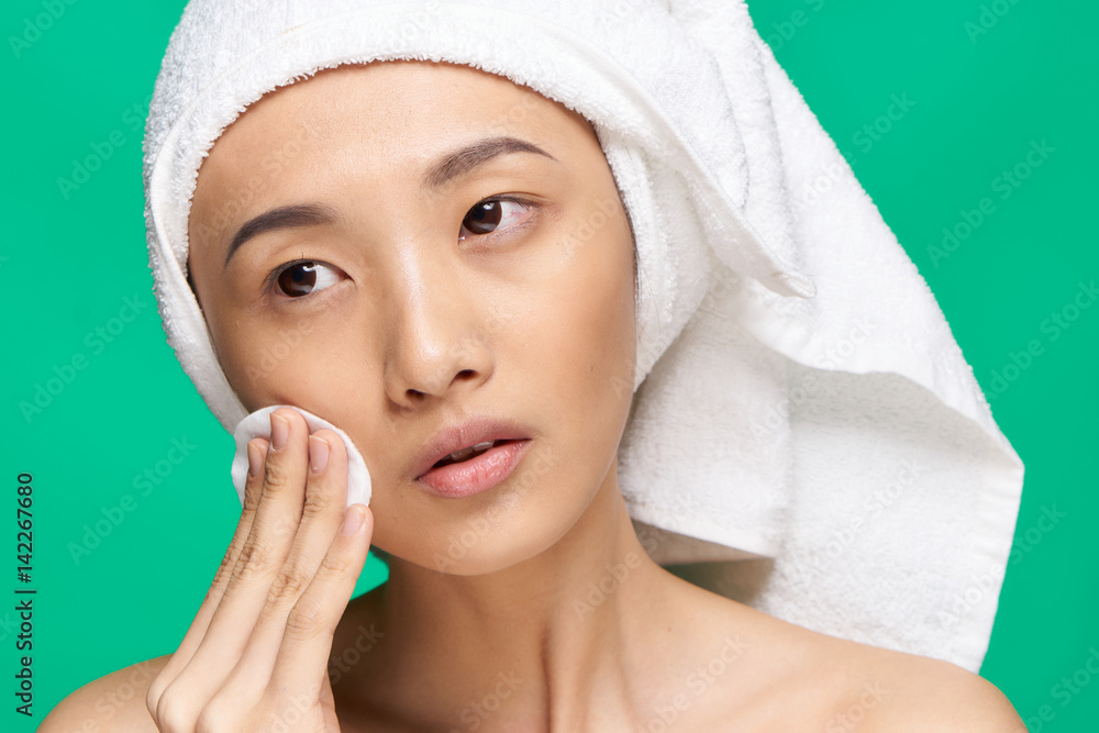 pretty woman on a green background wiping her face with a cotton disc pretty woman on a green background wiping her face with a cotton disc