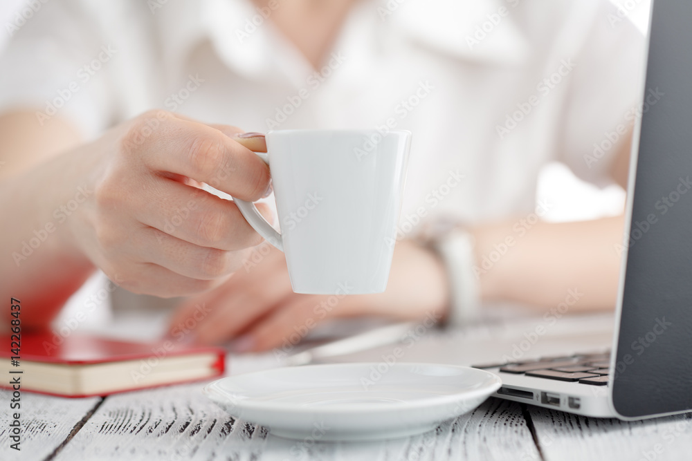 Female designer hands holding cup of hot beverage and working with laptop. Employee woman drinking morning tea of coffee. Coffeebreak during working day, creative people Female designer hands holding cup of hot beverage and working with laptop. Employee woman drinking morning tea of coffee. Coffeebreak during working day, creative people