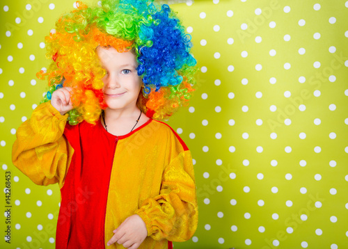 Fotografija A cheerful clown in an iridescent wig and huge boots stands on a luscious bright