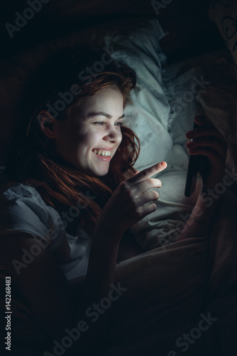 happy woman looking in the phone lying on the bed
