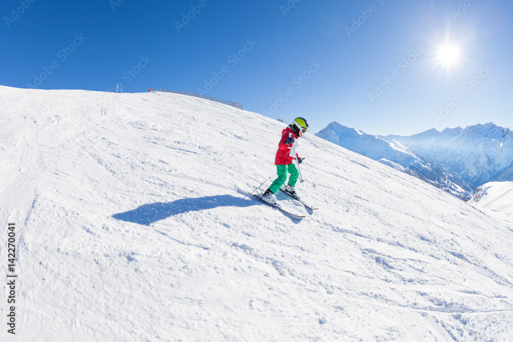 Little skier walking down the hill at sunny day
