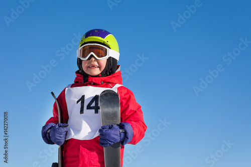 Happy boy holding skis in hands against blue sky