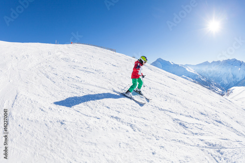 Little skier walking down the hill at sunny day