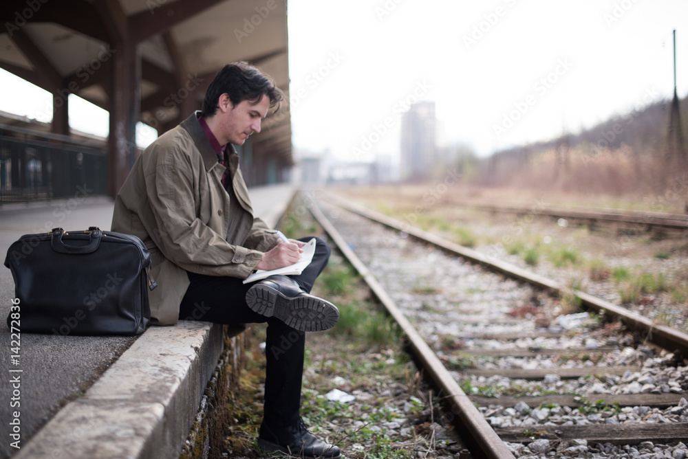Writer sitting on rail station and writing a letter
