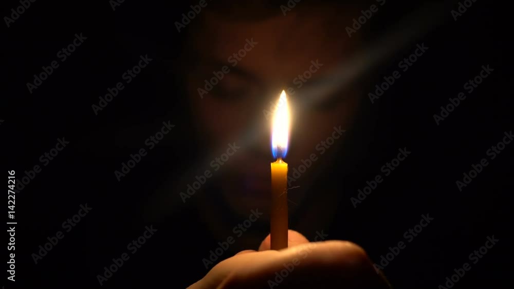Young caucasian man in dark room hold a candle in front his face and with close eyes. Pray for Young caucasian man in dark room hold a candle in front his face and with close eyes. Pray for