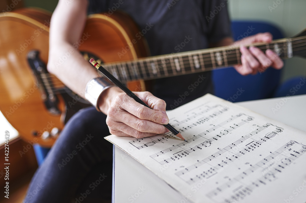Fototapeta premium a person making notes on sheet music and holding a guitar.