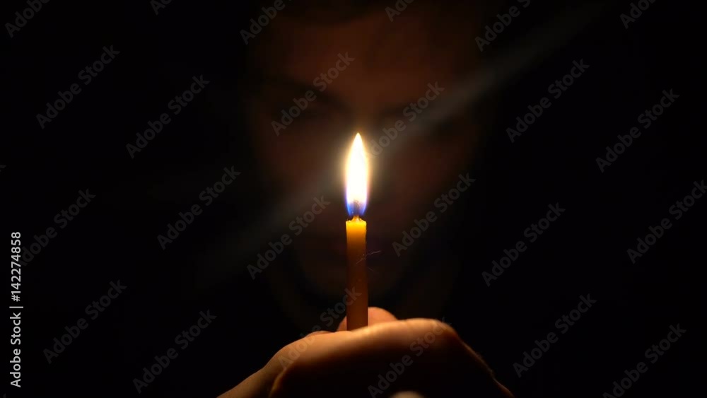 Young caucasian man in dark room hold a candle in front his face and looking to camera Young caucasian man in dark room hold a candle in front his face and looking to camera