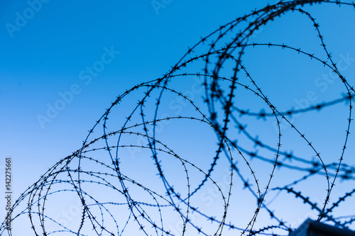 Top of fortress concrete security wall topped with barbed wire against blue sky background - view from prison and  freedom concept 