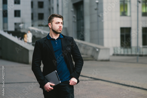 Outdoor portrait of a young businessman with modern tablet in hand against the background of the business center. Business concept
