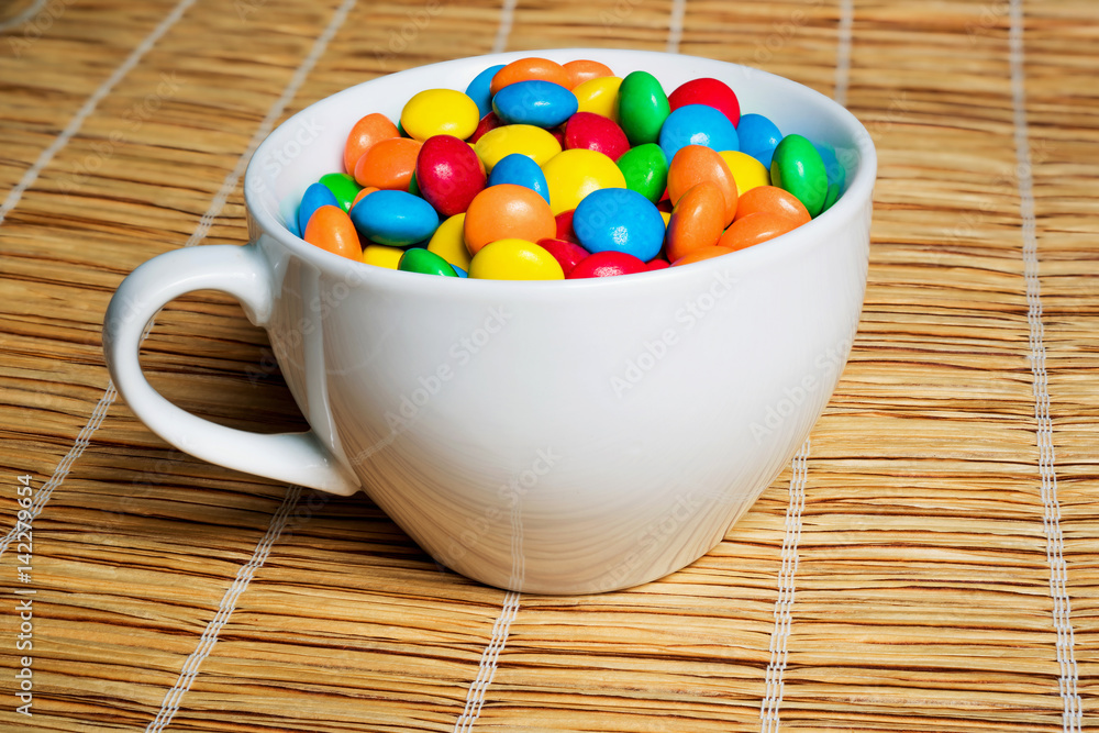 A cup with colorful tasty dragee on mat A cup with colorful tasty dragee on mat