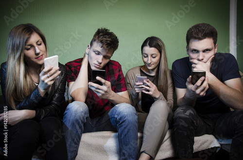 Group of teenagers and young adults staring at smartphones and not communicating with each other, anti social concept. Selective focus on girl on the right 