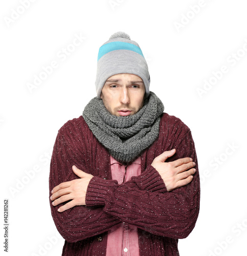 Young man in warm clothes shivering from cold on light background photo