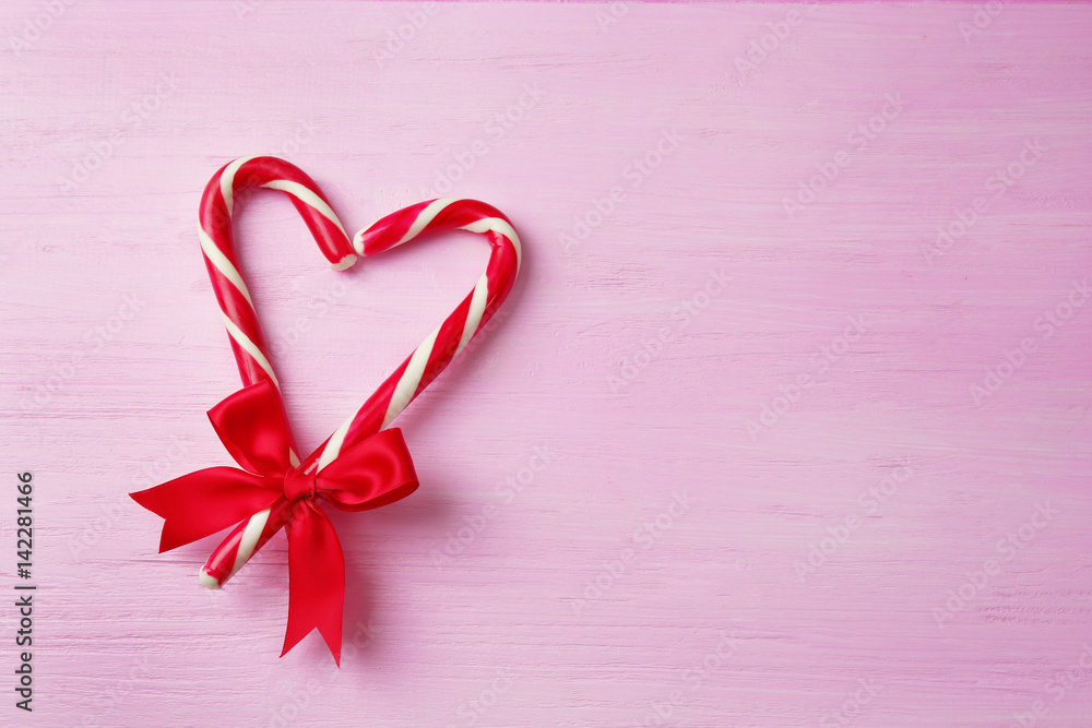 Heart shape made with candy canes on color wooden background Heart shape made with candy canes on color wooden background