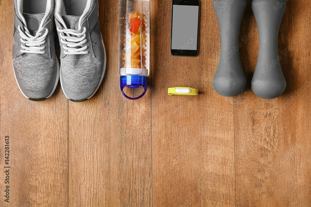 Fitness tracker and sports clothing with dumbbells on wooden floor, top view