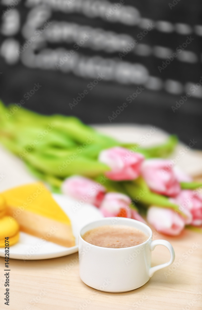 Cup of coffee, tasty cake and beautiful bouquet of flowers on table in cafe Cup of coffee, tasty cake and beautiful bouquet of flowers on table in cafe