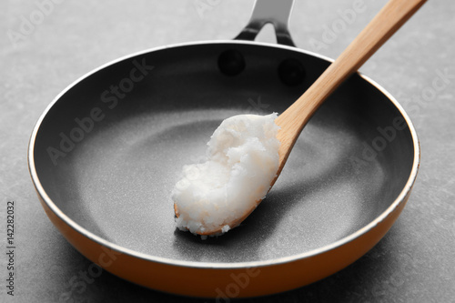Wooden spoon with coconut oil on frying pan