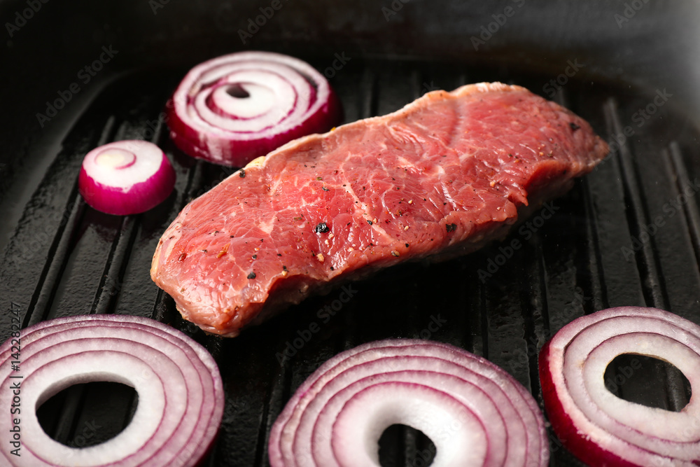 Preparing of steak with onion rings on grill pan, closeup