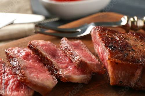 Sliced pieces of delicious medium rare steak on wooden board