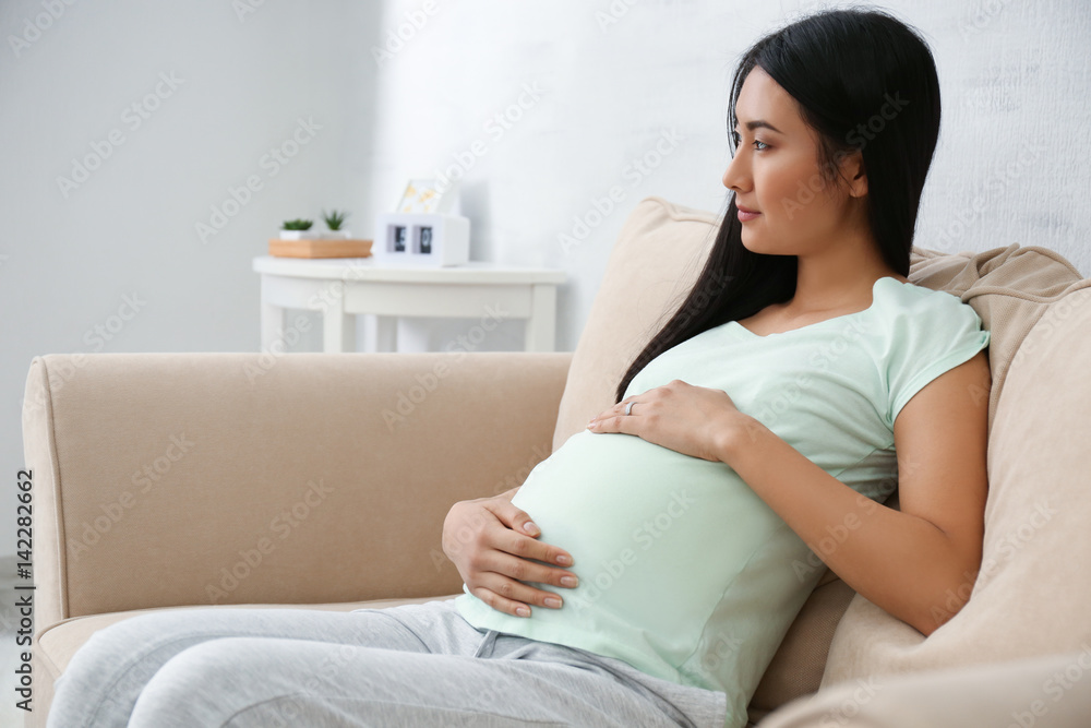 Pregnant Asian woman sitting on sofa at home Pregnant Asian woman sitting on sofa at home