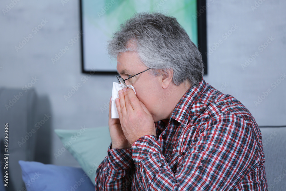 Senior man blowing nose on tissue at home Senior man blowing nose on tissue at home
