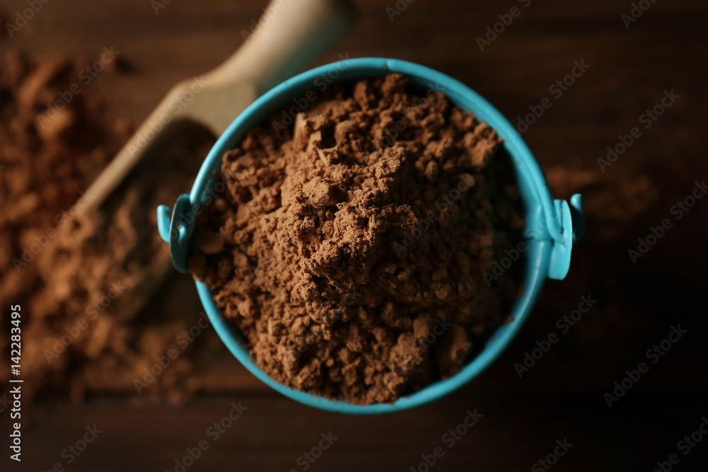 Small decorative bucket with cocoa powder on wooden background