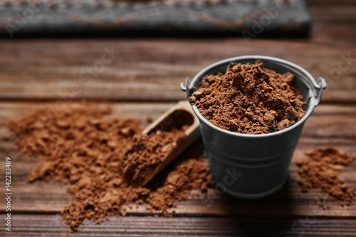 Small decorative bucket with cocoa powder on wooden background