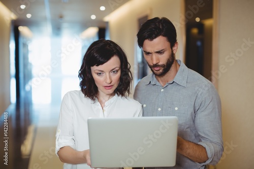 Male and female business executives using laptop in corridor