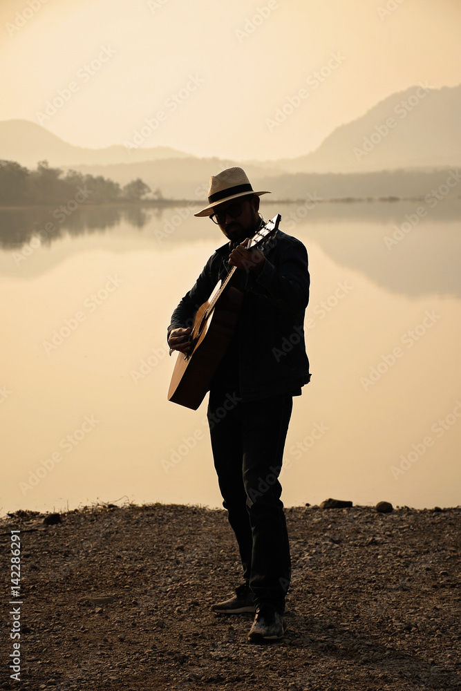 Obraz premium The young man guitarist The nature of the reservoir in the early morning.