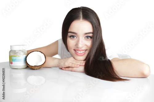 Beautiful young woman with jar of coconut oil on white background