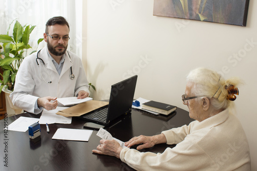 Obraz na płótnie Lekarz podaje zastrzyk w brzuch starej kobiecie. Lekarz geriatra przyjmuje pacjenta w gabinecie. Stara kobieta u lekarza geriatry.Lekarz geriatra przyjmuje pacjenta. Odbiera dokumenty od pacjentki. w salonie