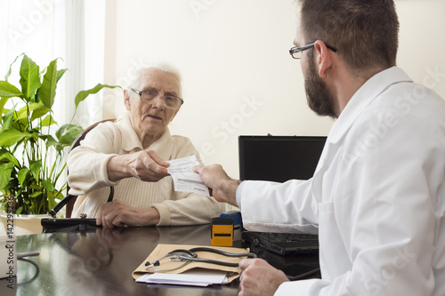 Lekarz geriatra przyjmuje pacjenta w gabinecie. Lekarz podczas pracy. Lekarz podaje pacjentce receptę.