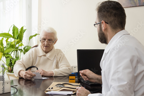Gabinet lekarski. Lekarz przyjmuje pacjenta. Pacjentka, stara kobieta czyta zapis na recepcie wystawionej przez lekarza. photo
