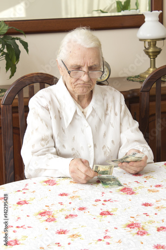 Emerytura. Stara kobieta liczy pieniądze. Stara kobieta ze smutną miną liczy pieniądze siedząc przy stole.