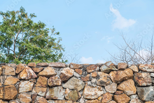 Closeup stone brick fence with blurred tree and blue sky textured background