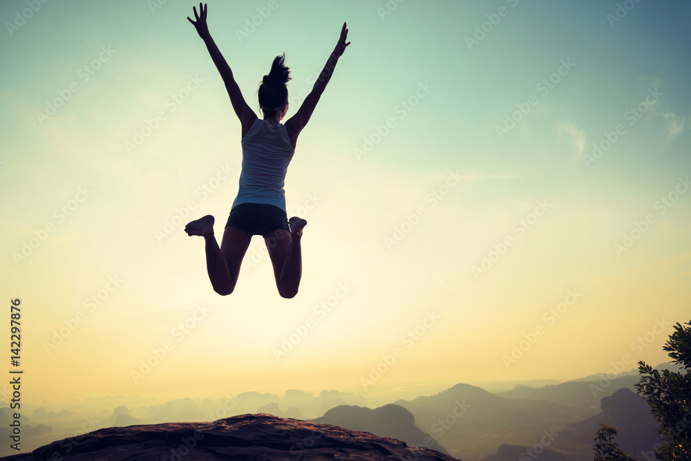 young woman jumping on sunrise rocky mountain peak, freedom, risk, challenge, success concept