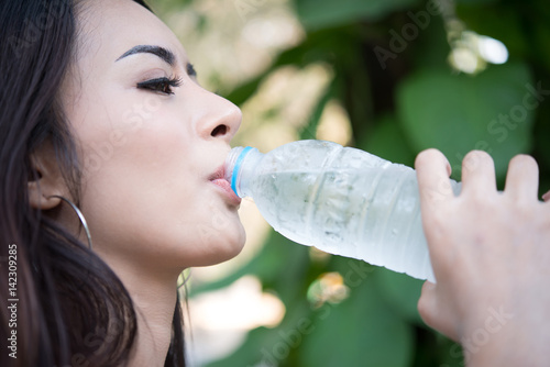 Young beautiful woman relaxing outdoors drinking water in the park.