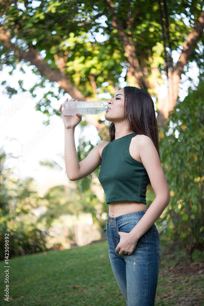 Young beautiful woman relaxing outdoors drinking water in the park.