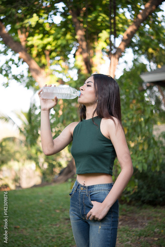 Young beautiful woman relaxing outdoors drinking water in the park.