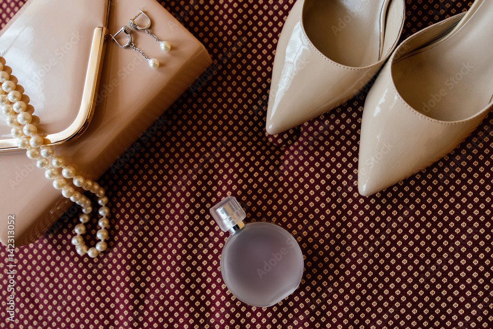 Bride's shoes, garter, perfume, necklace and clutch on burgundy cloth surface Bride's shoes, garter, perfume, necklace and clutch on burgundy cloth surface